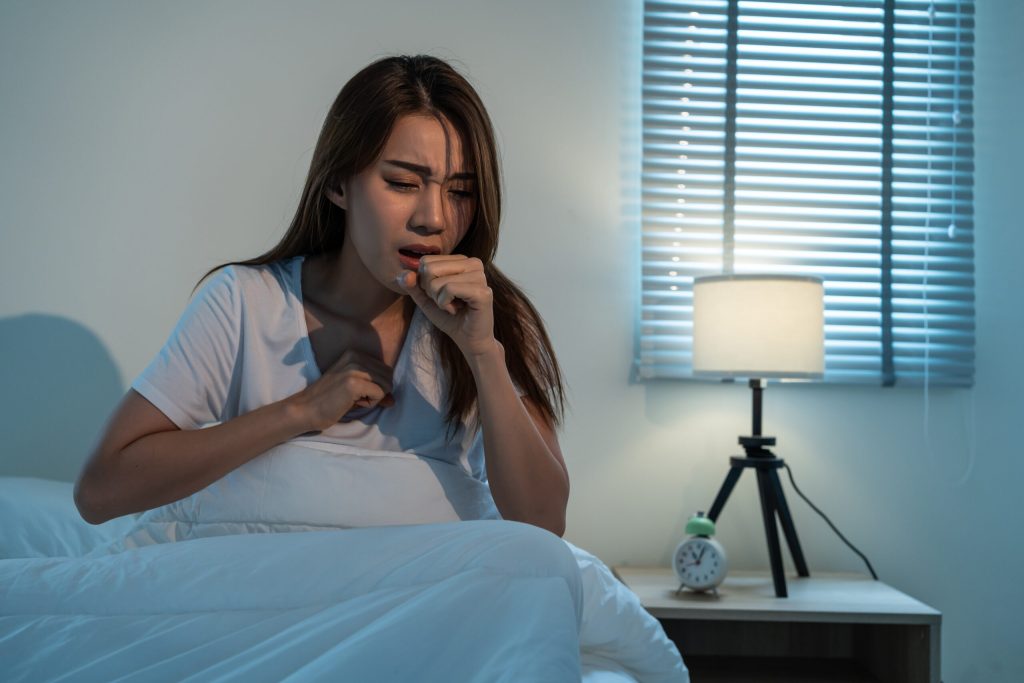 Asian beautiful girl in pajamas feel sick while sit on bed in bedroom.