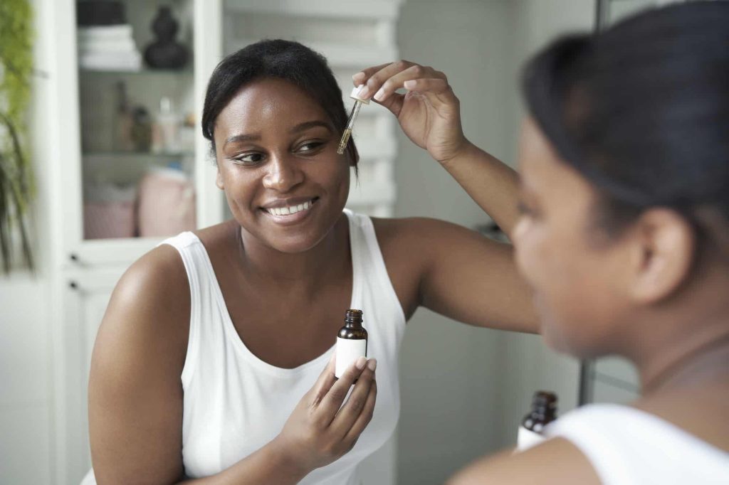 Afroamerikansk kvinne som bruker serum til ansikt på badet