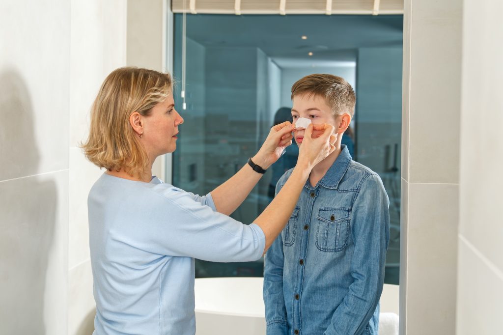 mamma limer et plaster for å fjerne hudormer til sønnen.