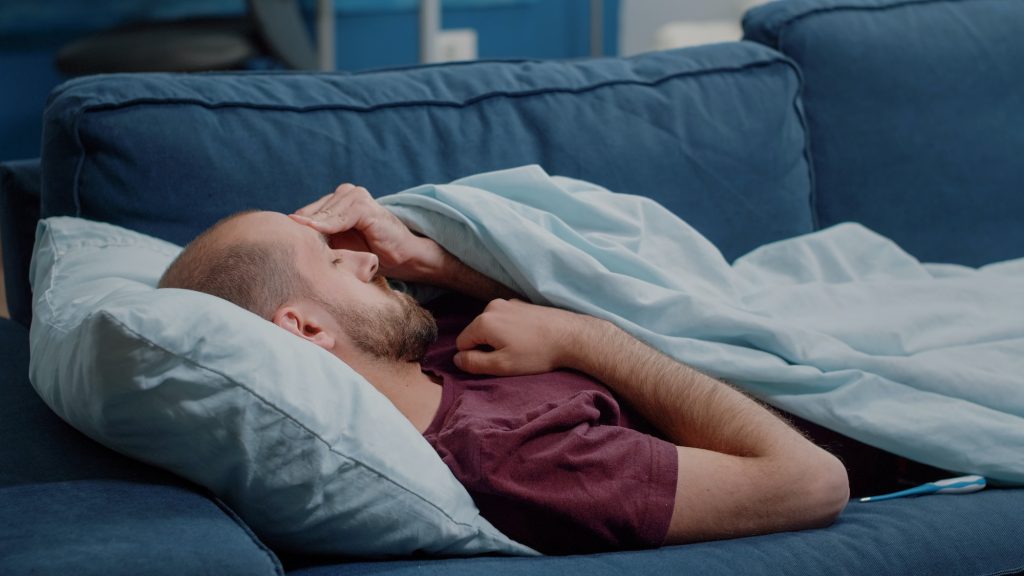 Sick man looking at thermometer to check fever measurement