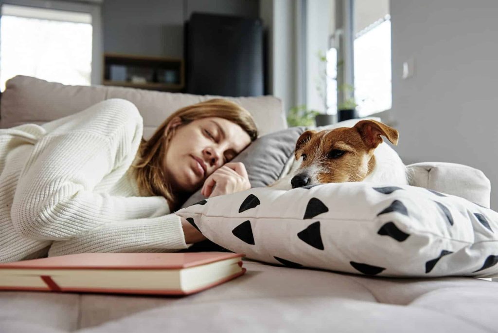 Dame sover på sofaen med en hund. Hunden ser ut til å ha skabb.
