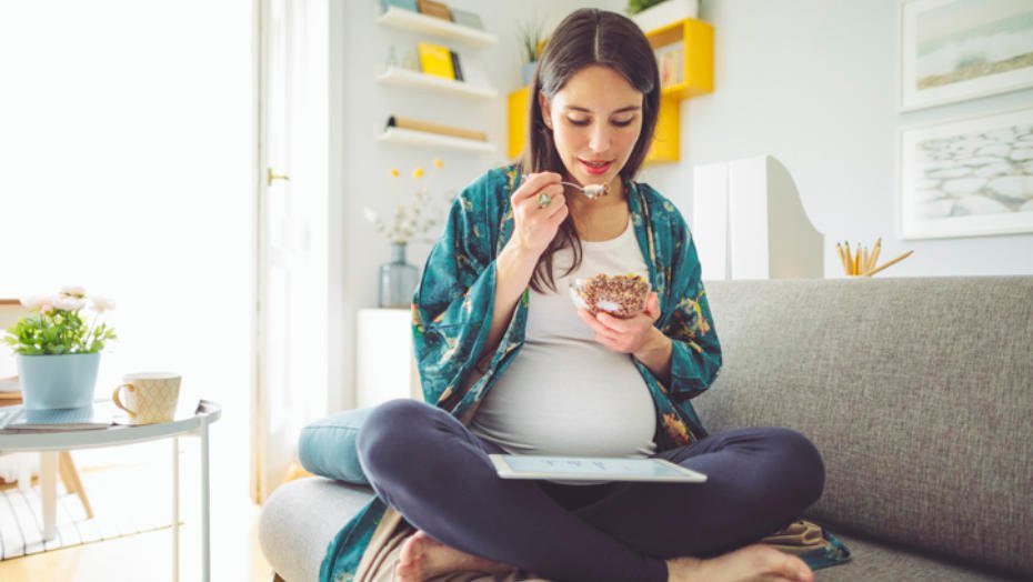 En ung gravid kvinne spiser yoghurt og musli en tidlig morgen.