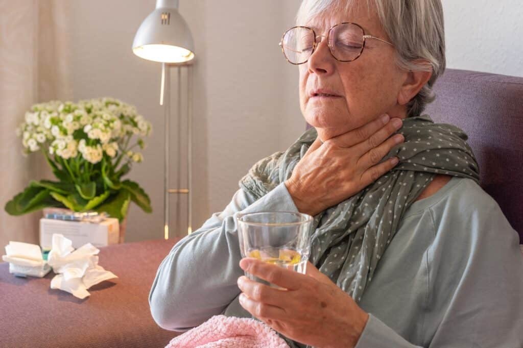 Elderly adult caucasian woman with sore throat and fever as seasonal flu or pollen allergy