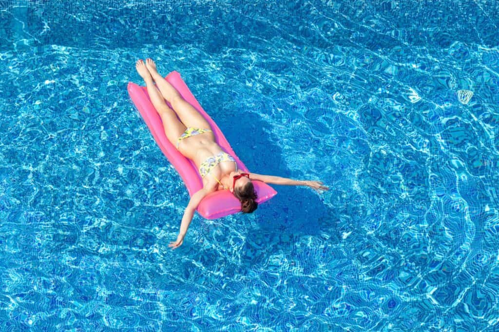 sexy brunette woman tanning on inflatable mattress in swimming pool