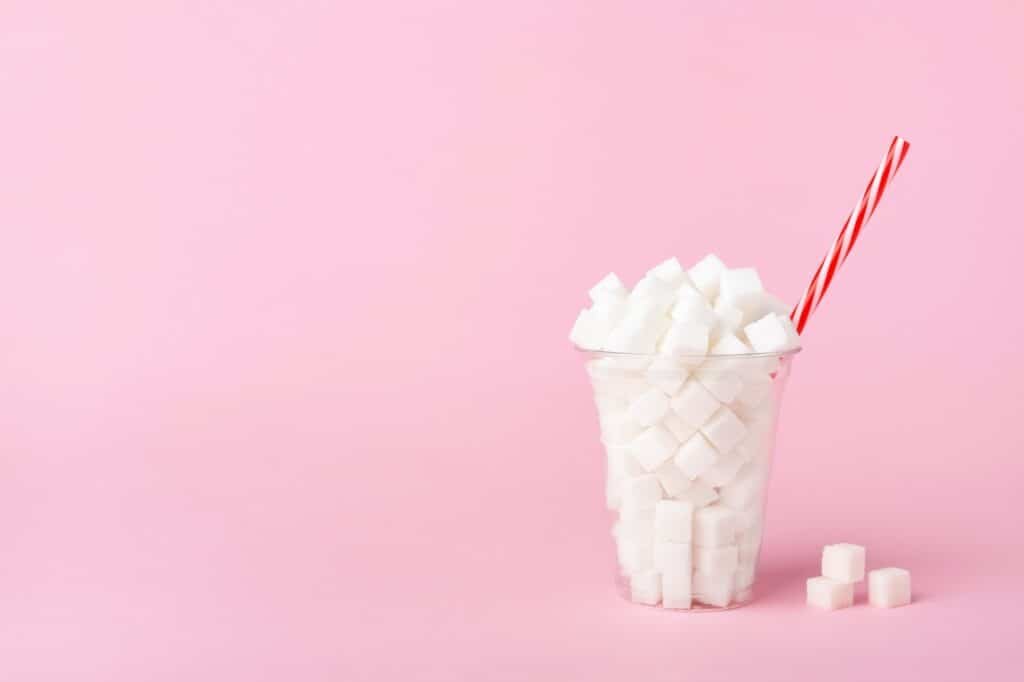 Shake Glass Full of Sugar Cubes on Pink Background, Unhealthy Drink Concept