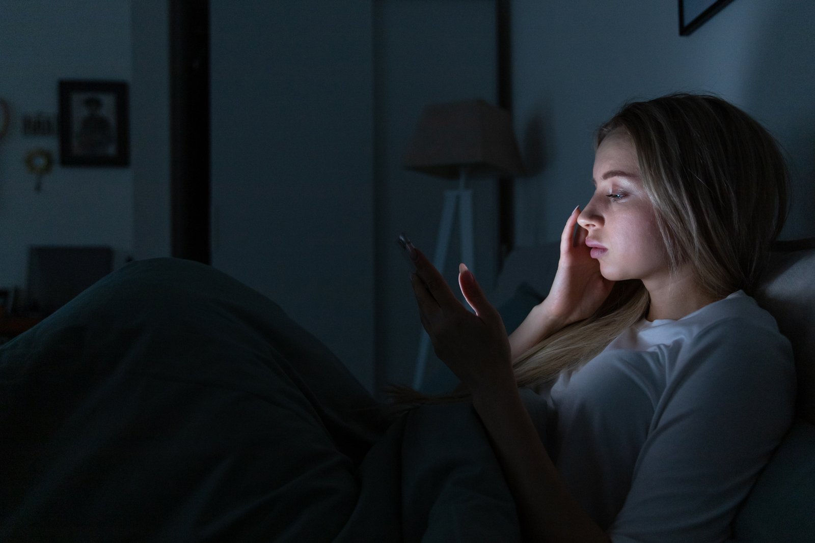 Sleepy exhausted woman lying in bed using cellphone chatting in social networks, bored can not sleep