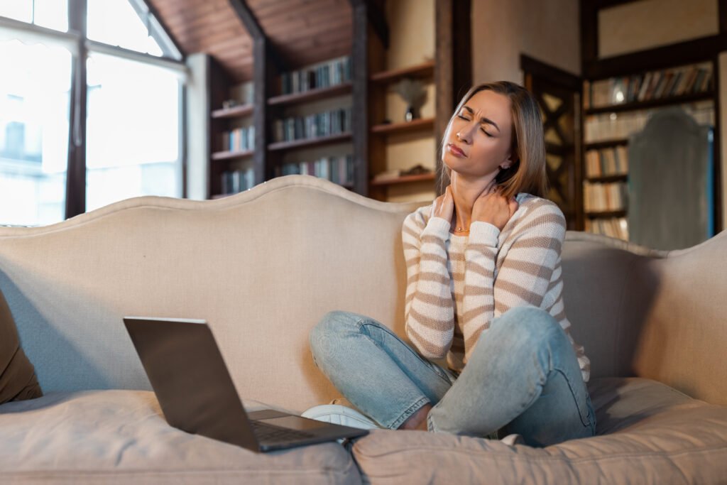 Tired woman sitting on couch with pc, massaging neck