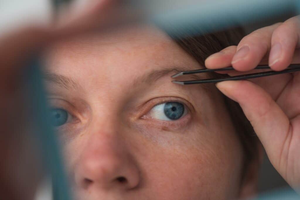 Woman plucking eyebrows by the window