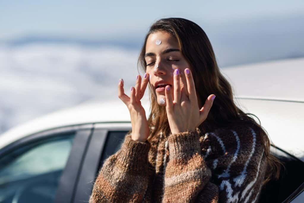 Young woman applying sunscreen on her face in snow landscape