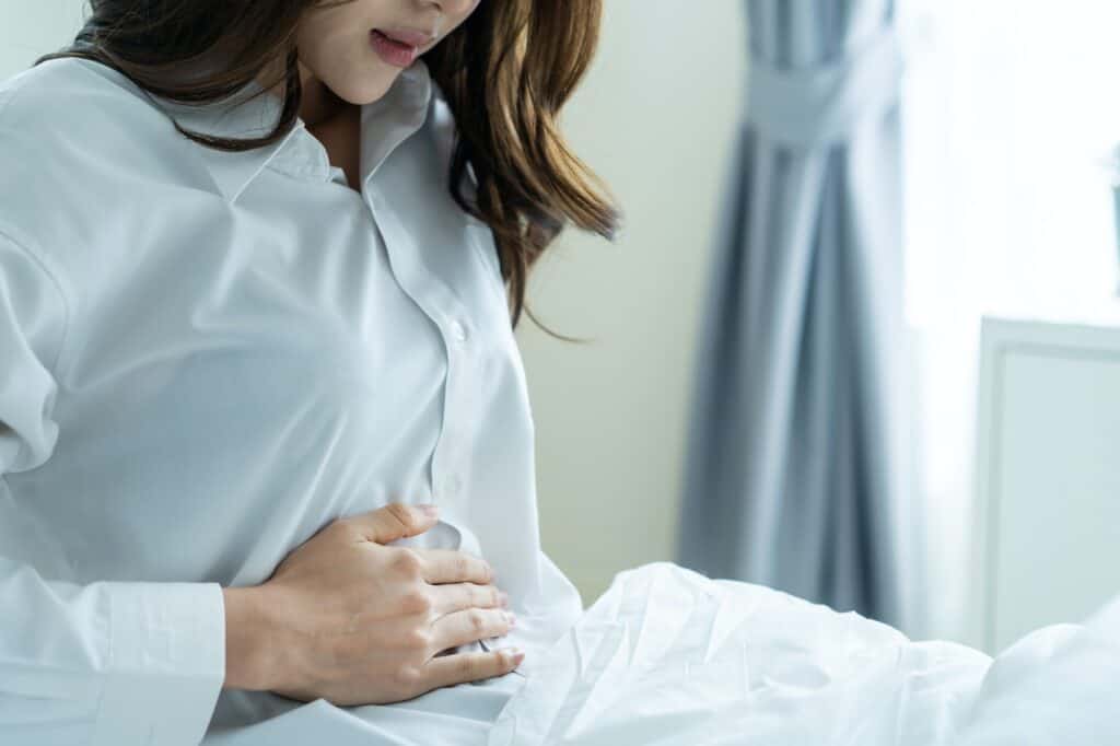 Asian young woman feel painful after wake up, having stomach ache or periods then clasping belly