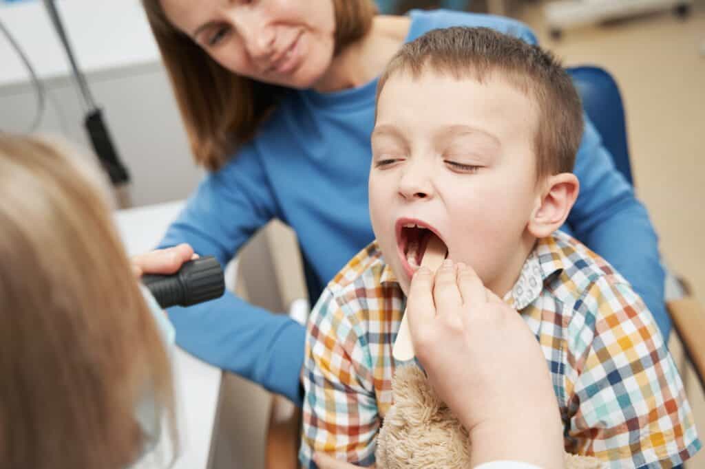 Pediatrician examining child throat with tongue depressor