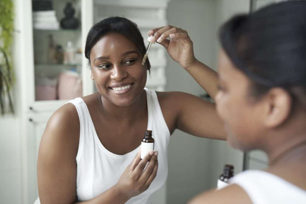 African-American woman using serum to face in the bathroom