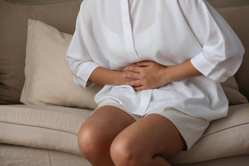 A sick woman suffering from stomachache, abdominal pain while sitting on sofa at home