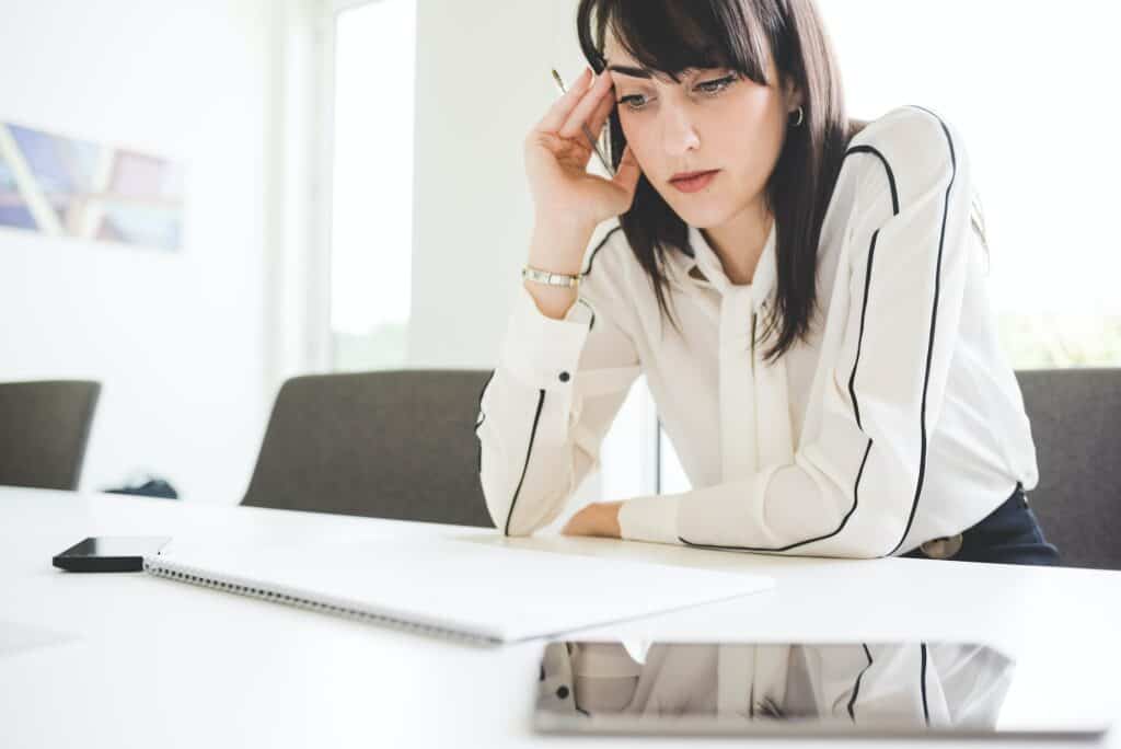 Stressed young businesswoman at office desk with notepad