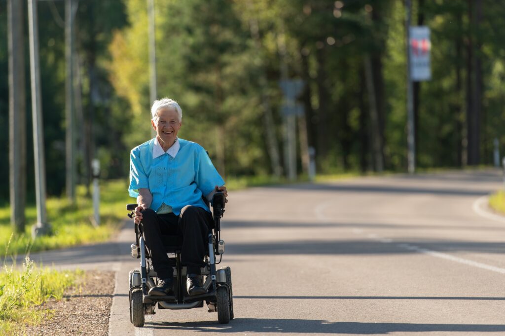 Smilende funksjonshemmet gammel kvinne i rullestol på motorveien. Trygt.