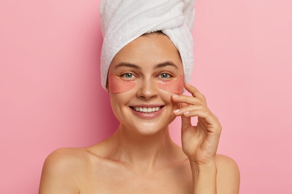 Smiling attractive European woman with glad face expression, wears pink silicone pads under eyes, ha