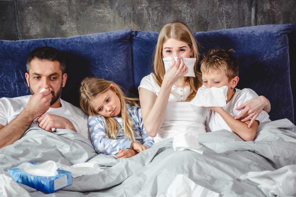 Family of four has a flue and lying on bed together