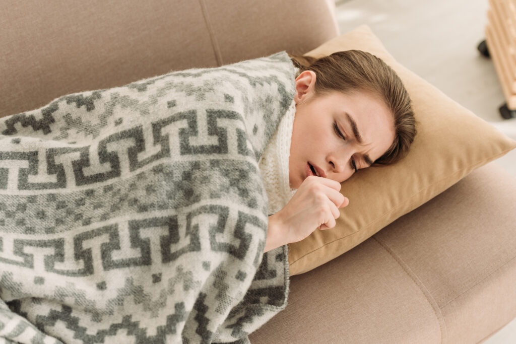 diseased girl coughing while lying on sofa under blanket