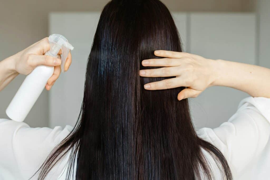 Brunette young woman applying hair spray on hair.Close up