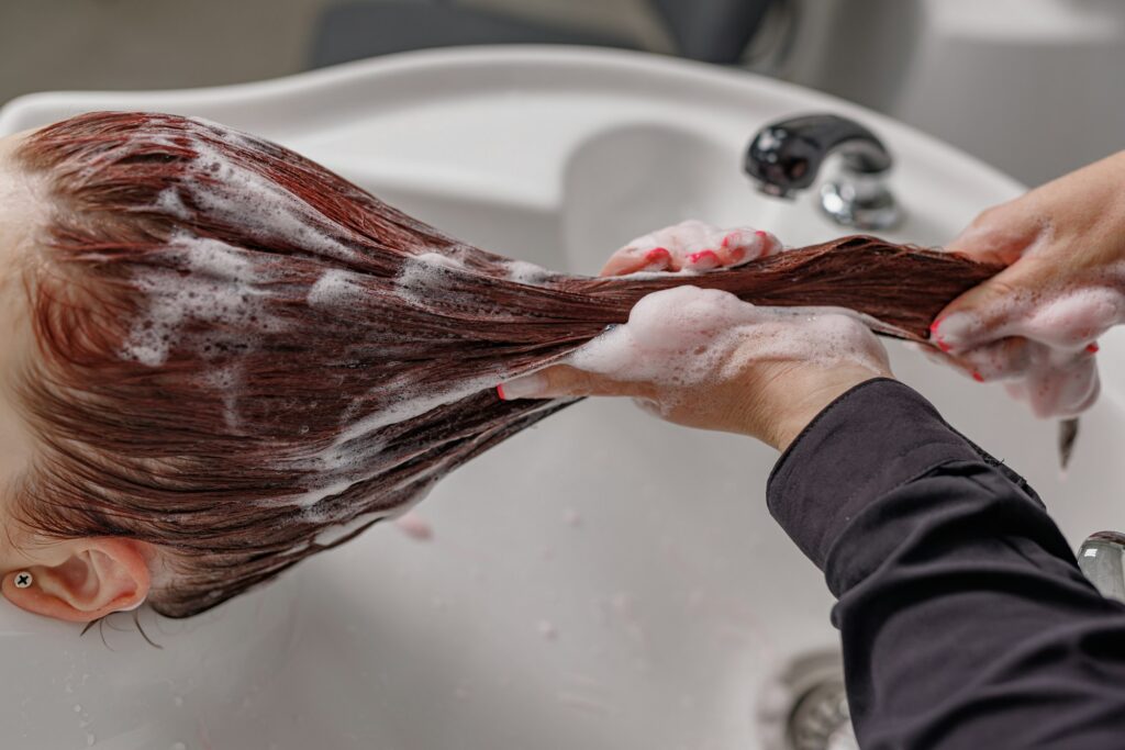 professional hairdresser washes hair with shampoo to client in beauty salon