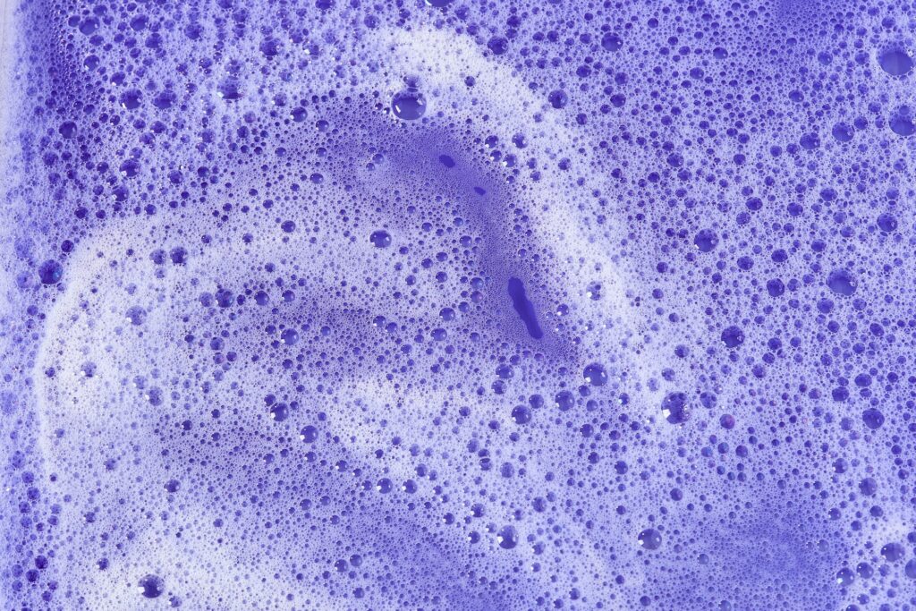 Soap and shampoo foam on purple and blue background. Seamless detergent in water texture.