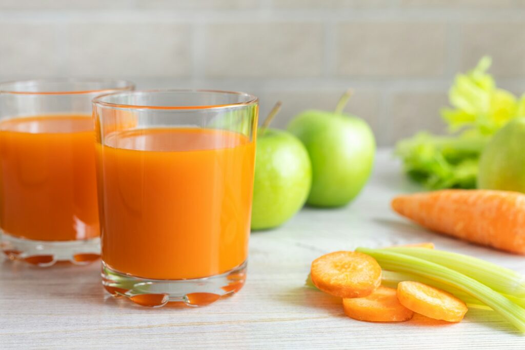 Two glasses with carrot juice, celery and green apple on the table.