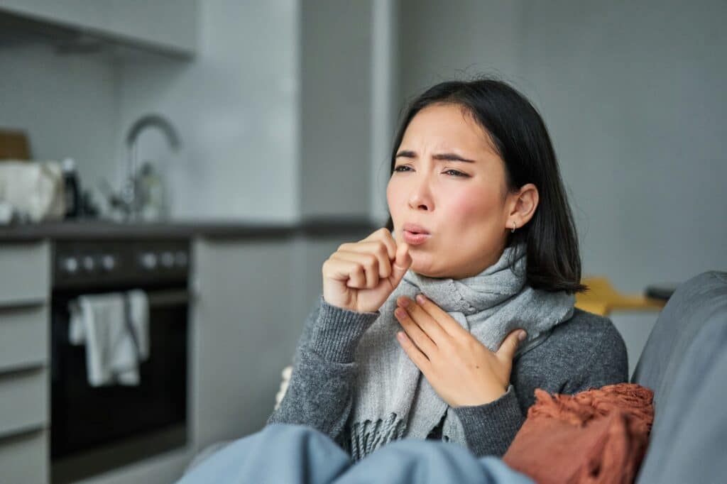 Sick korean woman coughing and feeling unwell, grimacing, has influenza, cought cold or flu