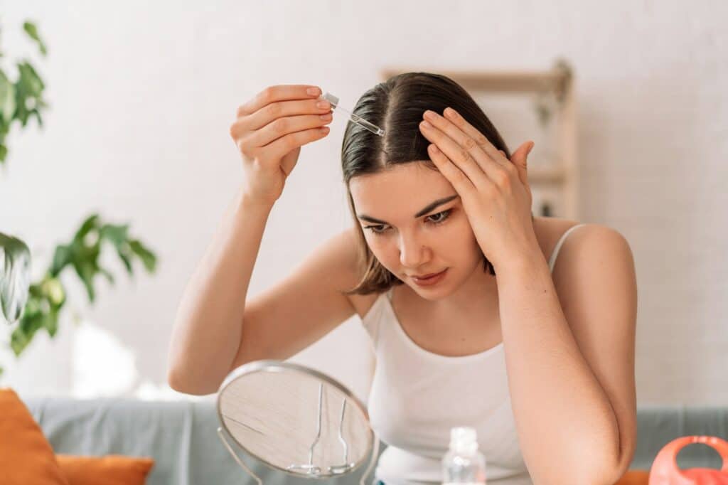 Lady sitting on the couch looks in the mirror and drips hair oil with a pipette on her hair