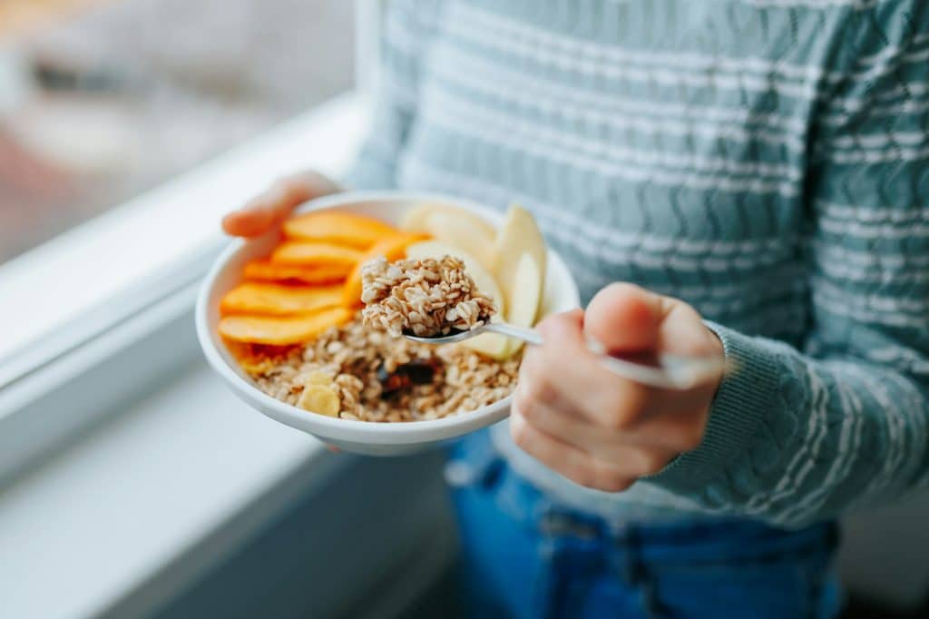 Young woman with muesli bowl, girl eating breakfast cereals nuts, pumpkin, oats and apple in bowl.