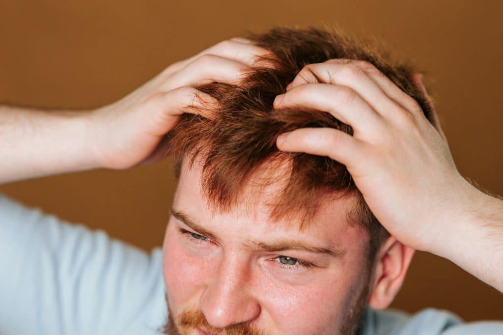 A studio shot of a guy with a head full of itchy hair, scratching his scalp in discomfort.