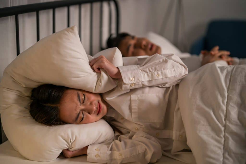 Asian woman feel frustrated from husband snoring while sleep at night.