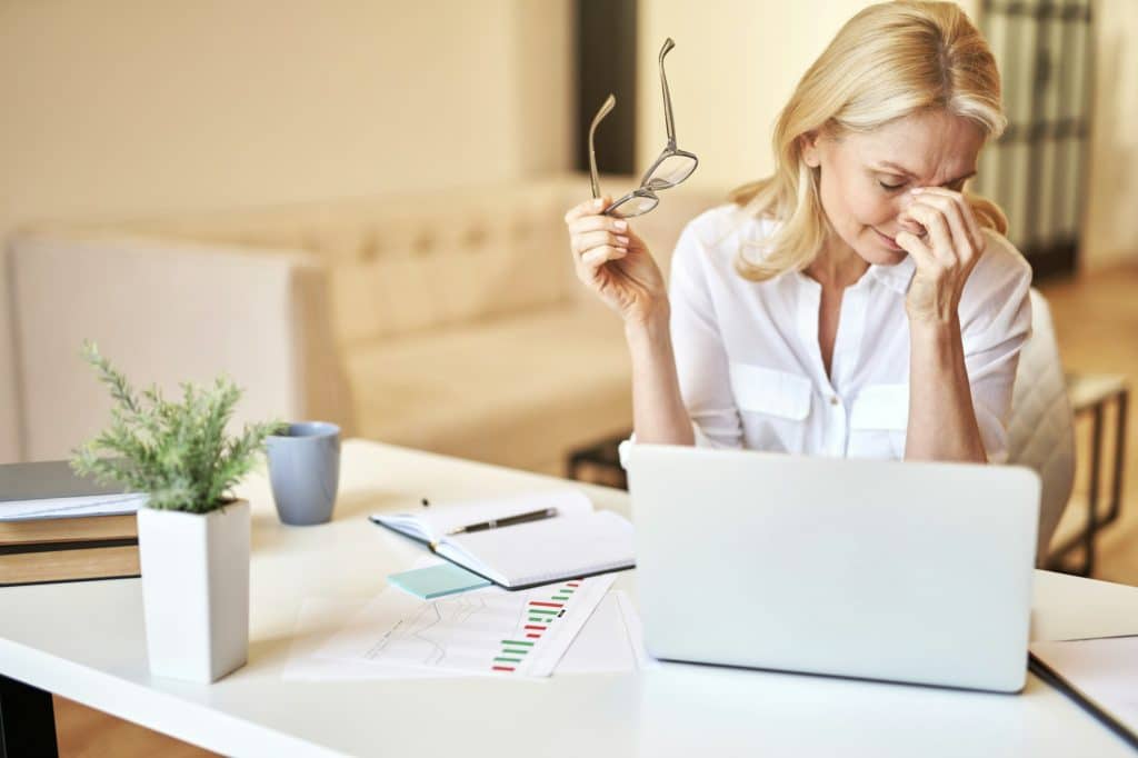 Tired mature businesswoman took off her glasses, massaging nose bridge, suffering from dry eyes